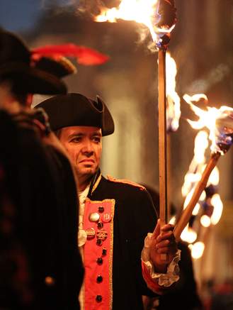 Original caption read: "A man with a flaming torch who is dressed in period apparel."